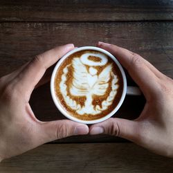 Directly above view of hands holding cappuccino cup with froth art