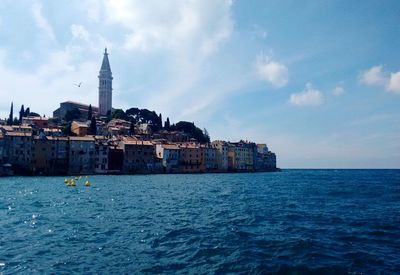 Buildings at waterfront against cloudy sky