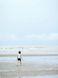 Rear view of little child on beach against sky