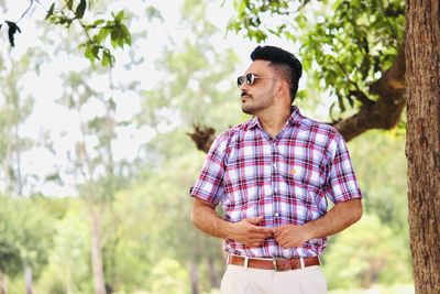 Man looking away while standing against trees