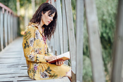 Woman reading book while sitting on footbridge