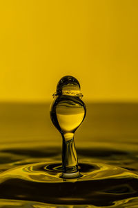 Close-up of drop splashing on water against yellow background