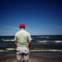 Rear view of man standing on beach against clear blue sky