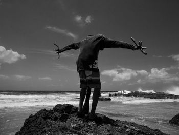 Rear view of man standing with arms outstretched on rock at rainbow bay