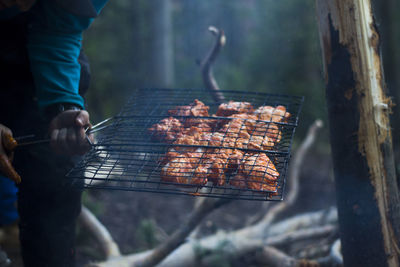 Midsection of man holding meat in metal grate at campsite