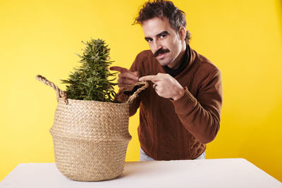 Side view of woman holding wicker basket against yellow background