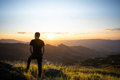 Rear view of man standing on mountain during sunset