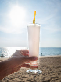 Close-up of hand holding drink at beach against sky