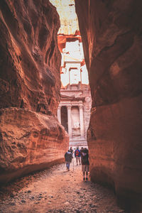 Rear view of people walking by rock formations at petra