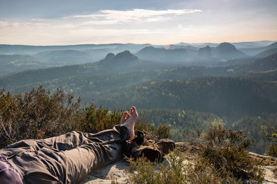 Low section of person relaxing on landscape against sky