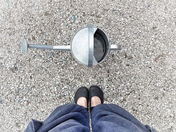 Low section of woman standing by watering can on pebbles