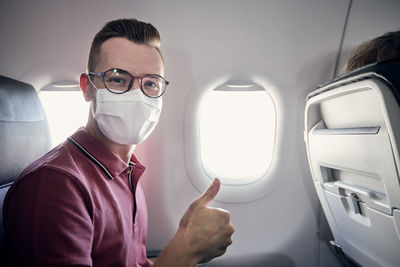 Portrait of happy tourist with face mask during flight. young man showing thumbs up in airplane.