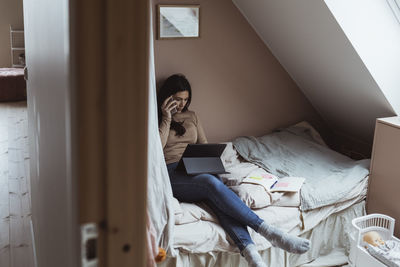 Businesswoman talking on smart phone while using digital tablet in bedroom