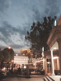 People on illuminated street by buildings against sky at dusk