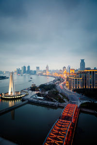 Illuminated buildings by river against sky in city