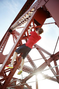 Low angle view of male athlete exercising on metal over footbridge in city during sunny day