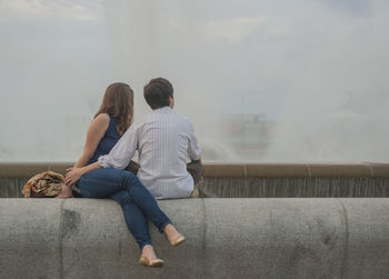 Young couple sitting on retaining wall of fountain