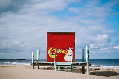 Red lifeguard hut on beach against cloudy sky