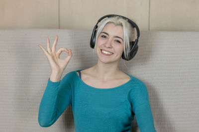 Portrait of smiling young woman gesturing ok sign while listening music at home