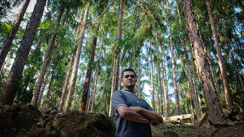 Low angle portrait of man standing against trees in forest