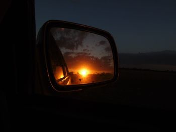 Close-up of side-view mirror against sky at sunset