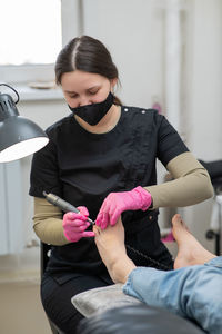 The pedicure master processes the client's foot using an apparatus with an abrasive disc