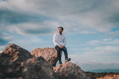 Full length of young man standing on rock against sky