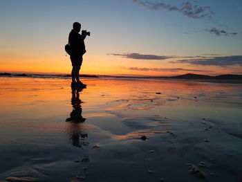 Silhouette man photographing sea against sky during sunset