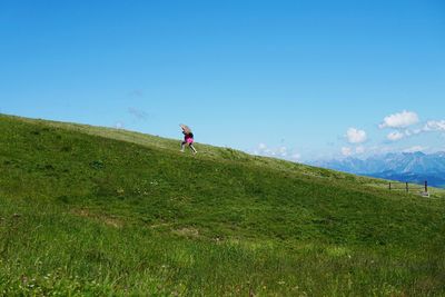 Person with umbrella walking uphill on grass against sky