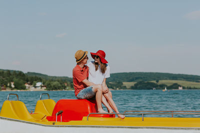 Cheerful man and woman in paddleboat on lake against sky