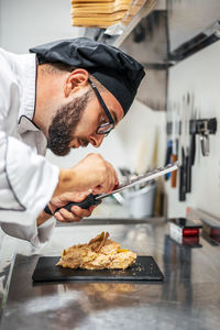 Side view of busy male cook using grater and garnishing sweet dessert placed on slate board in kitchen