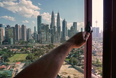 Close-up of hand holding cityscape against sky