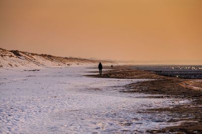 Person on snow covered land against clear sky during sunset