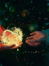 Cropped hands of woman giving illuminated string lights to friend