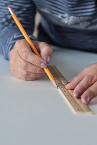 Midsection of man drawing line on white table using ruler and pencil