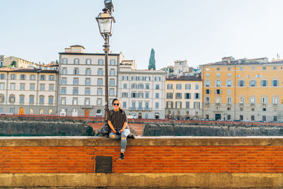 Portrait of woman sitting on retaining wall against buildings