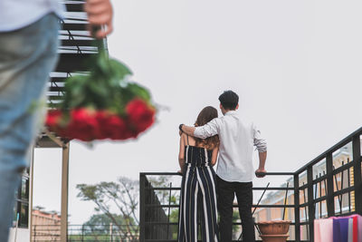 Rear view of couple standing by railing against sky