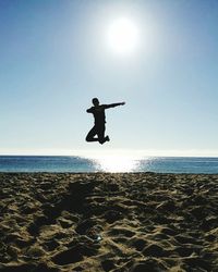 Full length of man jumping over beach against clear sky during sunny day