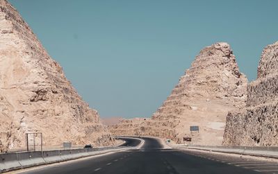 Empty road amidst rock formations against clear sky