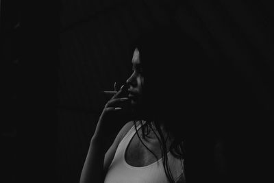 Young woman smoking cigarette against black background