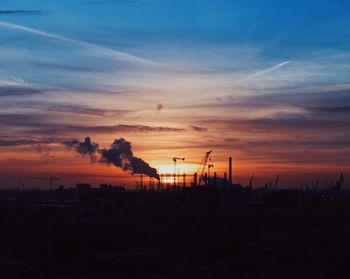 Silhouette cranes against sky during sunset