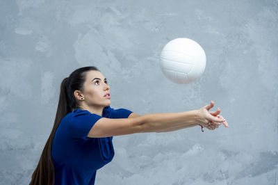 Side view of young woman playing volleyball against wall