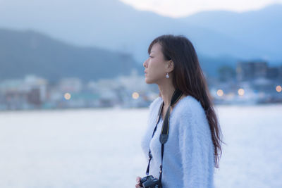 Young woman with camera standing at lakeshore