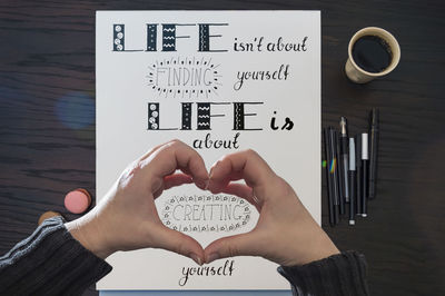 Close-up of person making heart shape paper over text at table