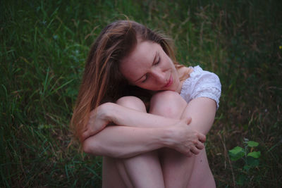 Woman with eyes closed hugging knees while sitting on grassy field