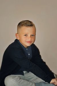 Portrait of boy sitting against gray background
