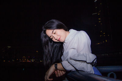 Smiling young woman looking down while standing in city at night