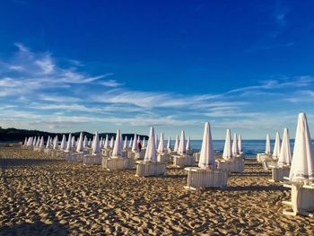 Closed parasols and lounge chairs at beach against blue sky