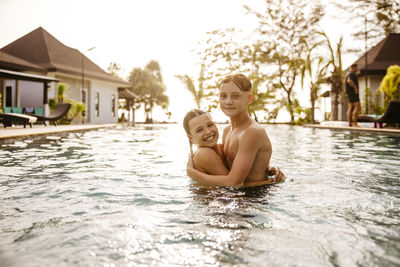 Portrait of brother and sister embracing in swimming pool at resort during sunset