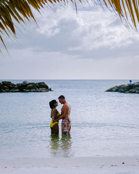 Couple embracing while standing at shore against sky